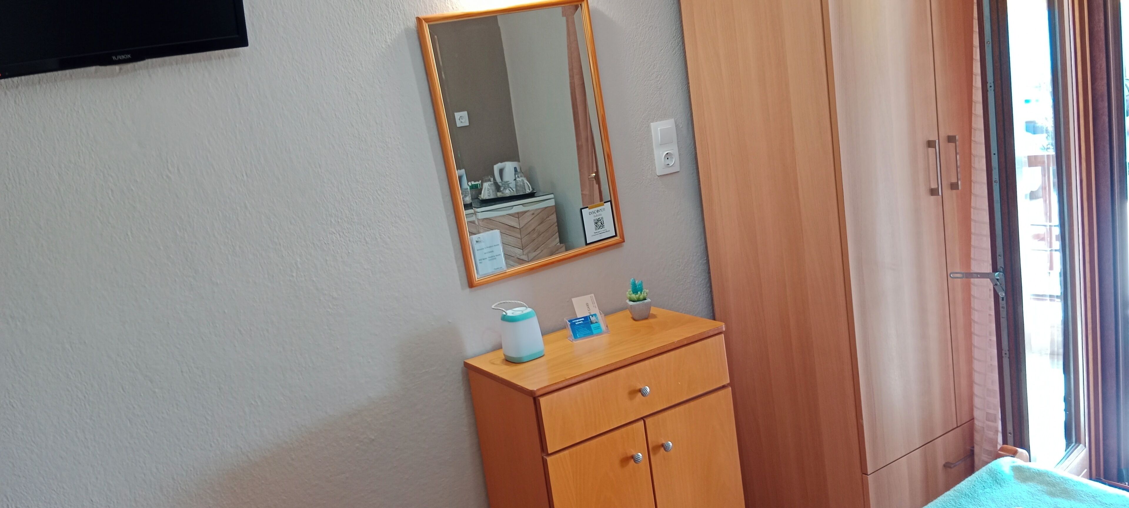 Un dormitorio con un armario de madera, una mesita de noche con artículos de aseo, un espejo y una ventana con cortinas.