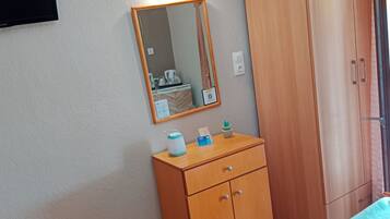 Un dormitorio con un armario de madera, una mesita de noche con artículos de aseo, un espejo y una ventana con cortinas.