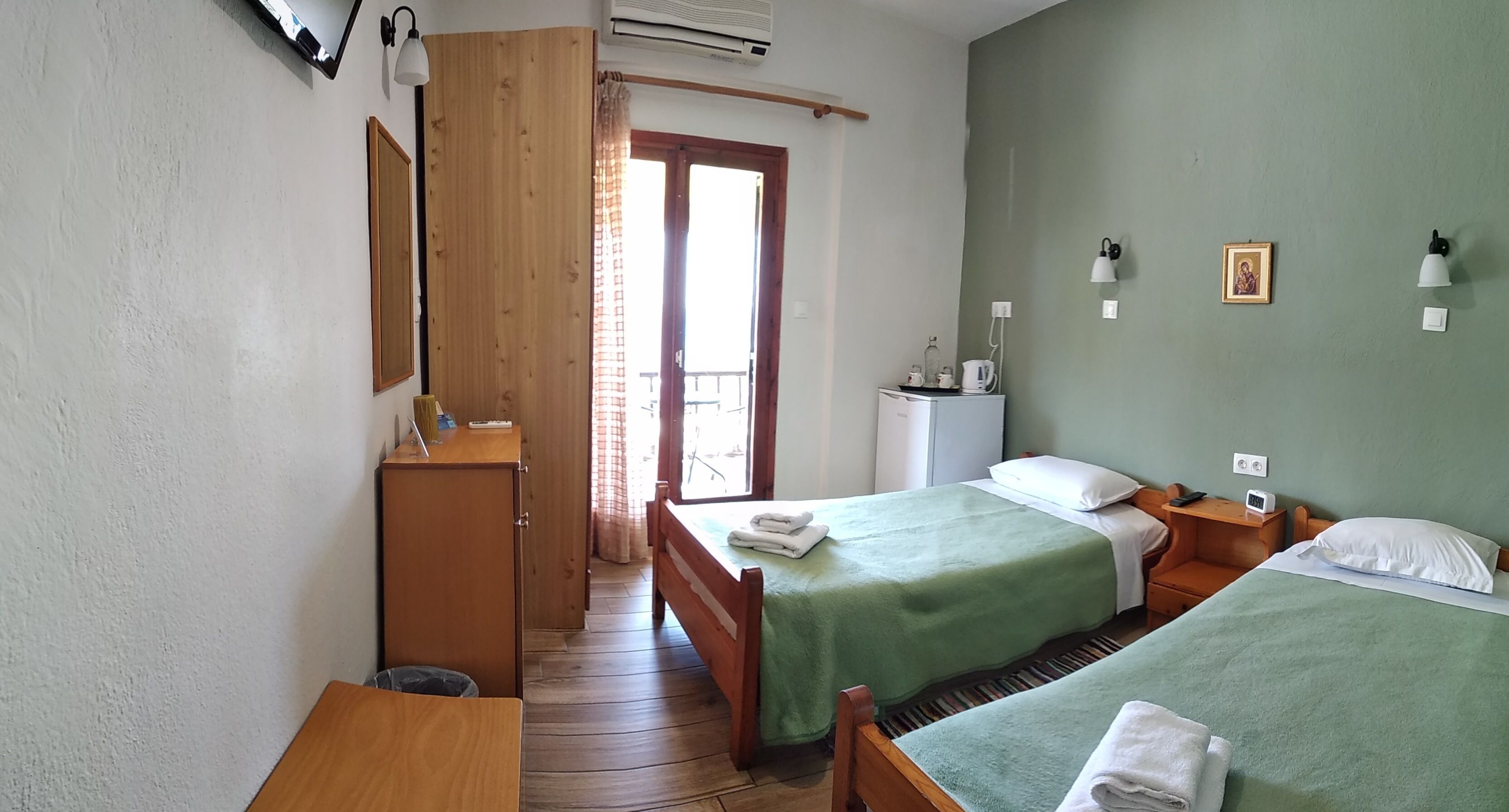 A room with two beds, a wooden wardrobe, a desk, and a window with curtains.