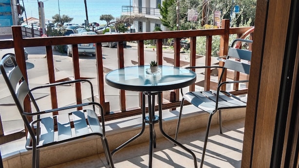 A balcony with a glass table and two chairs, overlooking a street with parked cars and buildings. - Prosforio Rooms (Aristotelis)