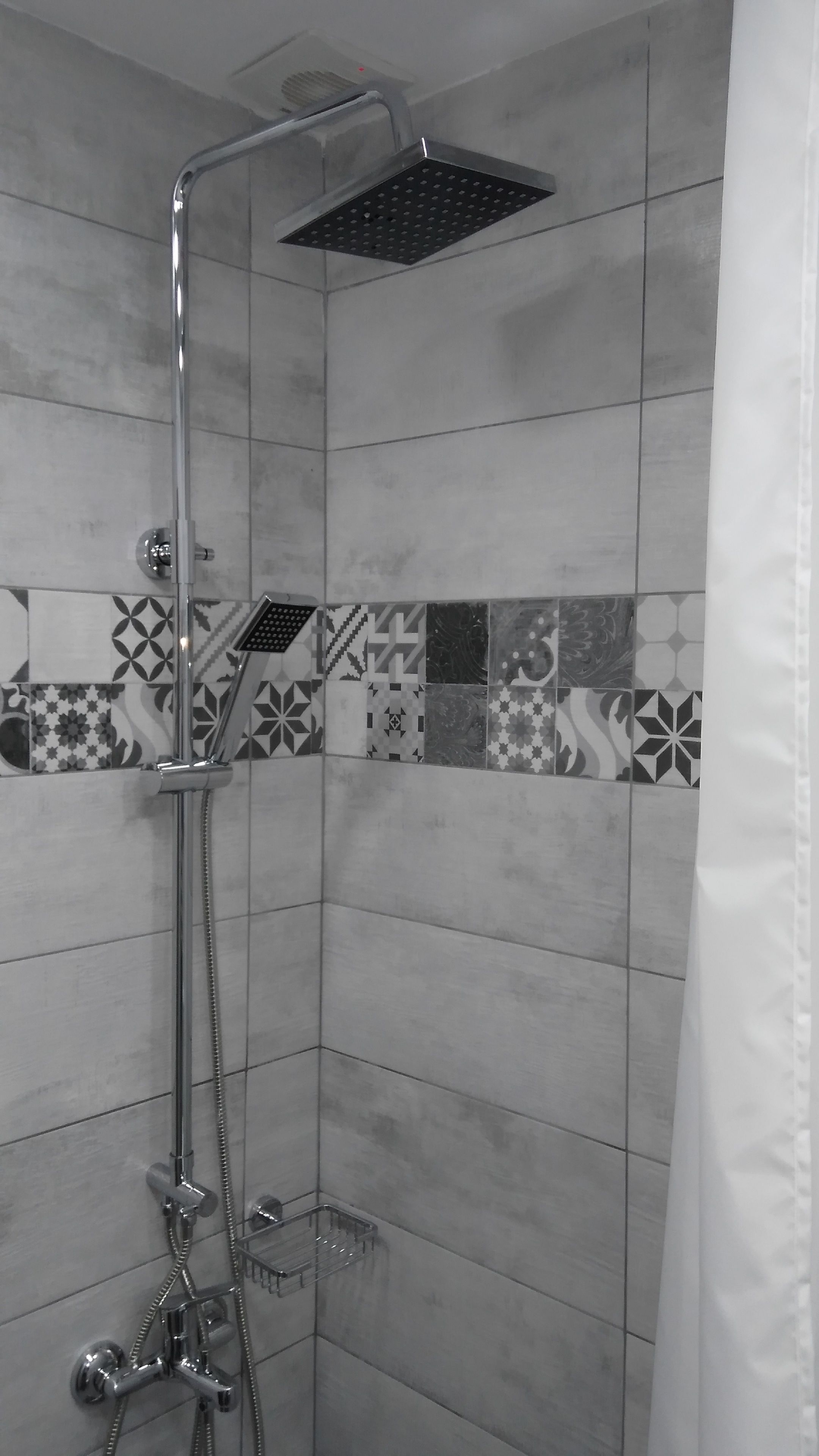 A shower with a handheld showerhead and a fixed showerhead, tiled walls with geometric patterns, and a shower curtain.
