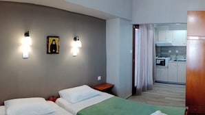 A hotel room with two beds, a kitchenette, and a bathroom visible through an open door. - Prosforio Rooms (Aristotelis)