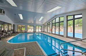 An indoor swimming pool with clear views of the outside, large windows, and a ceiling with skylights.