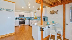 A kitchen with white cabinets, a central island with stools, a wooden ceiling, and a sign that reads "ACH HOME". - Oceanview Dog Friendly Home with Private Pool, Hot Tub, Elevator, and Game Room (Waves)