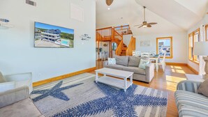 A spacious living room with a large window, a staircase, and a dining area. - Oceanview Dog Friendly Home with Private Pool, Hot Tub, Elevator, and Game Room (Waves)