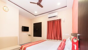 A hotel room with a bed, a TV mounted on the wall, an air conditioning unit, a ceiling fan, and a sign on the door. - OYO 9543 Rajarhat (Barasat)
