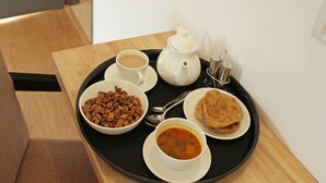 A tray with a cup of coffee, a bowl of cereal, a bowl of soup, a teapot, and a plate of flatbread on a wooden table. - OYO 9543 Rajarhat (Barasat)