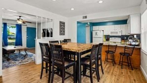 Une cuisine moderne avec des meubles blancs, une table à manger en bois et un mur d’accent bleu.