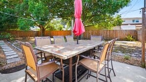 Une terrasse extérieure avec une table et des chaises, un parasol rose et une clôture en bois en arrière-plan.
