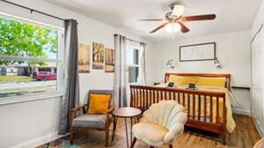 Une chambre à coucher comprenant un lit, une chaise, une petite table, un ventilateur de plafond et une fenêtre donnant sur l’extérieur.
