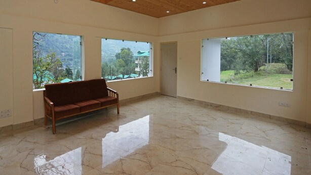 A spacious room with a wooden ceiling, large windows with views of greenery, and a marble floor. - OYO 9485 Swiss Camps (Kullu)