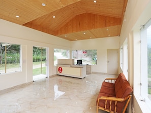 A spacious room with a wooden ceiling, a reception desk, a brown sofa, and large windows offering a view of greenery. - OYO 9485 Swiss Camps (Kullu)