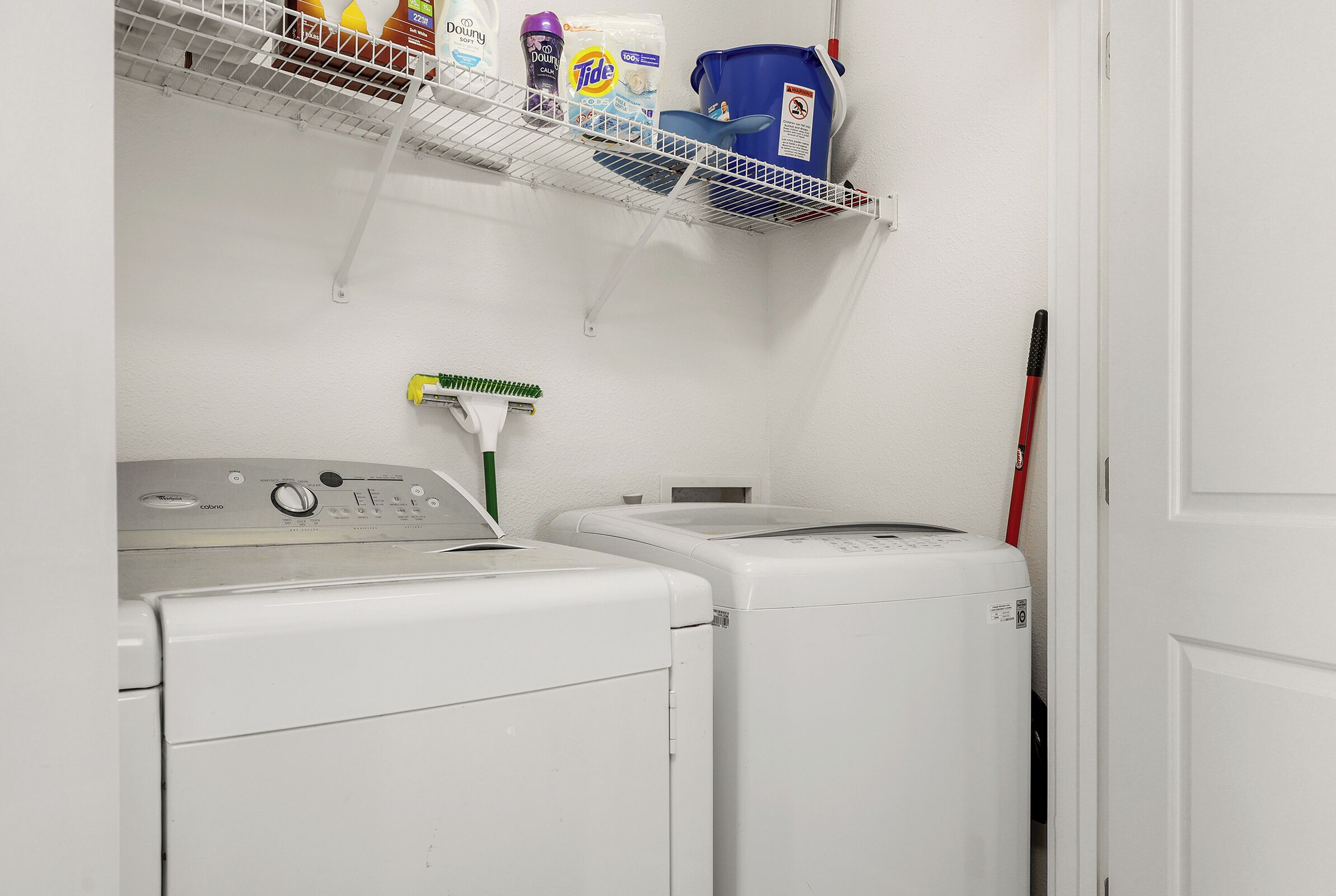 A laundry area with two washing machines, a shelf with cleaning supplies, and a broom.