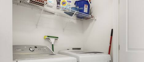 A laundry area with two washing machines, a shelf with cleaning supplies, and a broom.