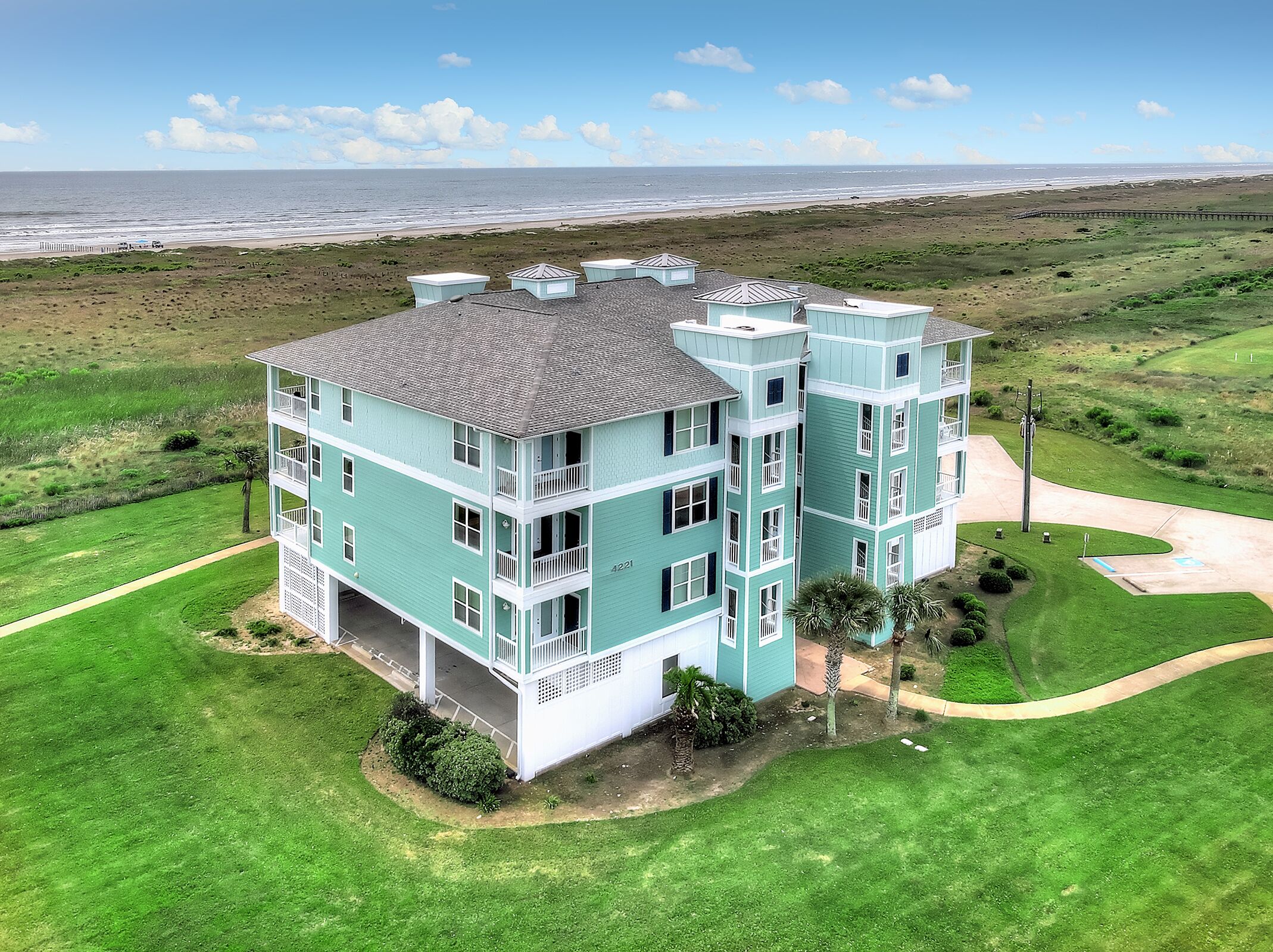 A multi-story building with a flat roof, located on a grassy area with a view of the ocean.