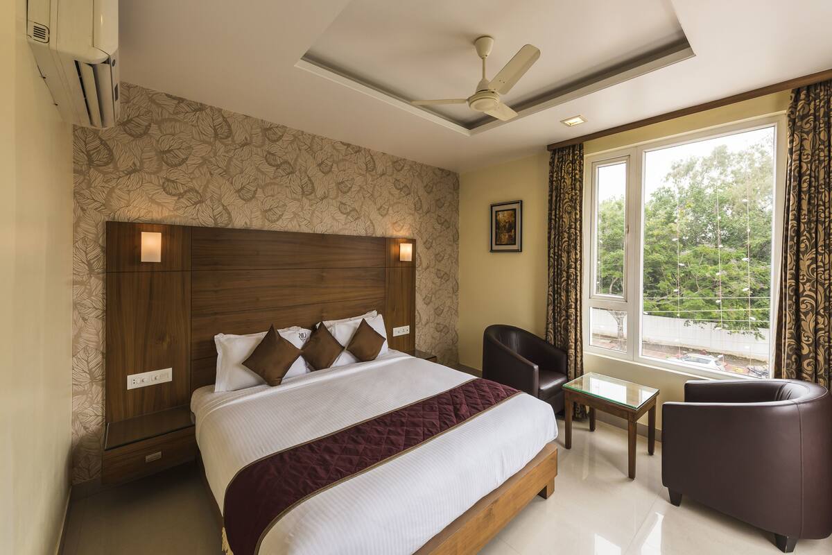 A hotel room with a large bed, a ceiling fan, a desk, a chair, and a window with curtains.