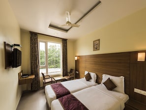 A hotel room with two beds, a desk, a chair, a TV mounted on the wall, and a window with curtains.