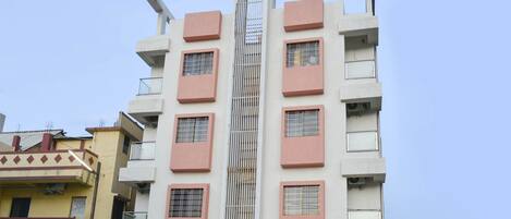 Un edificio moderno de varios pisos con una estructura vertical central, varios balcones y una variedad de estilos de ventanas.