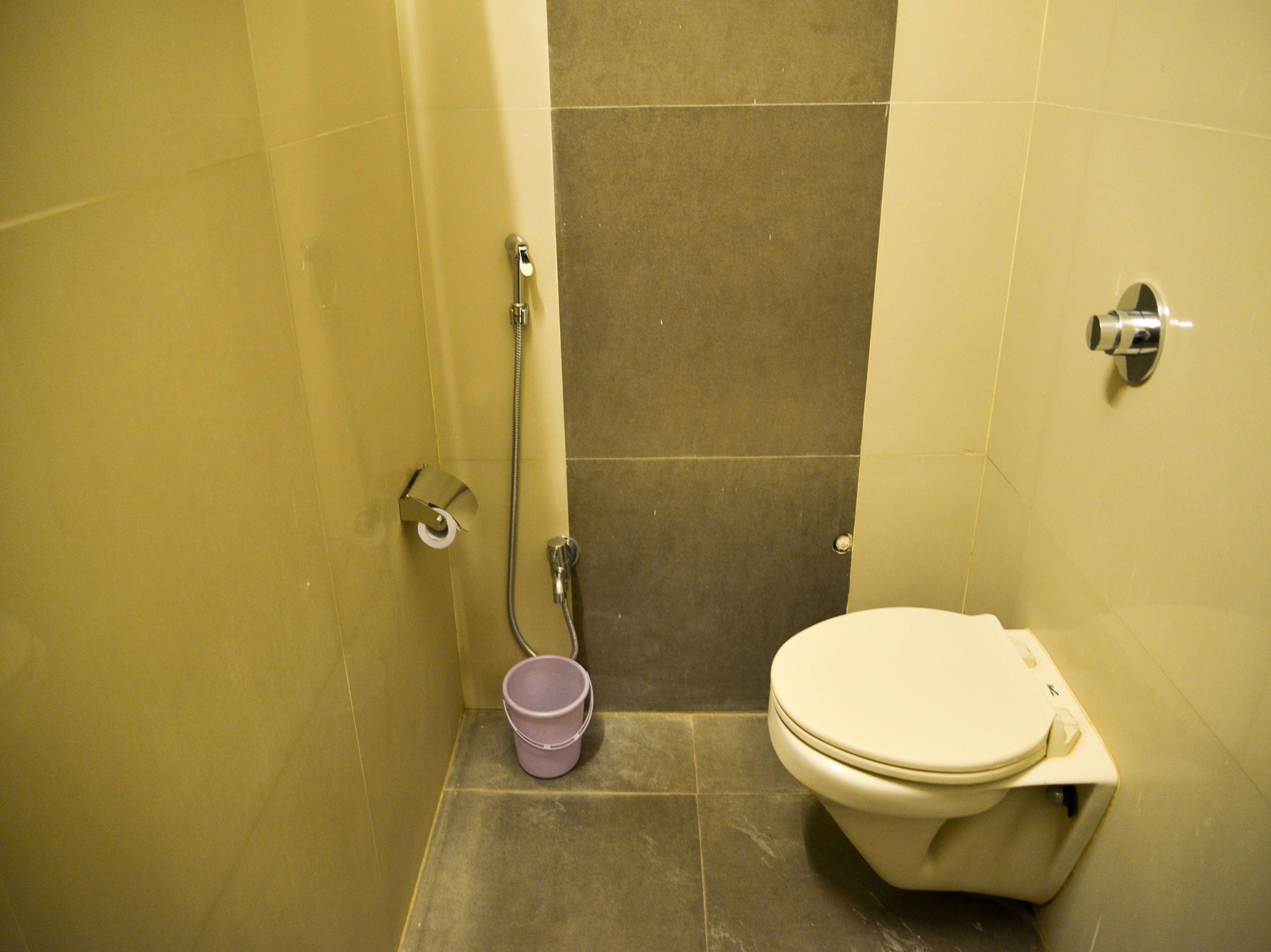 A small bathroom with a toilet, a shower, and a bucket.