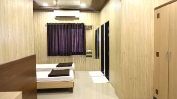 A hotel room with two beds, a wooden wardrobe, a mirror, and a ceiling fan.