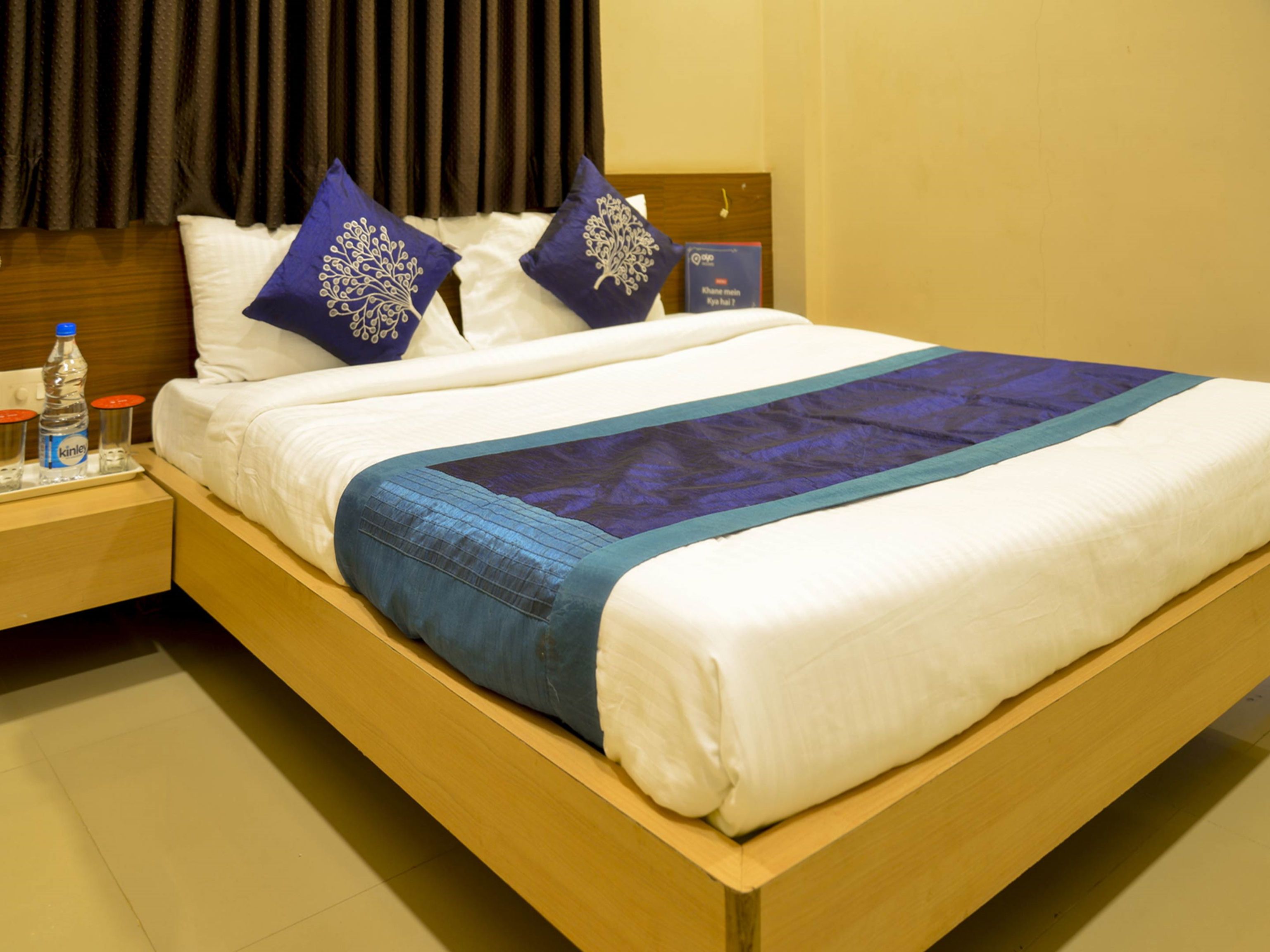 A neatly made bed with white and blue bedding, two decorative pillows, a water bottle, and a book on the nightstand.