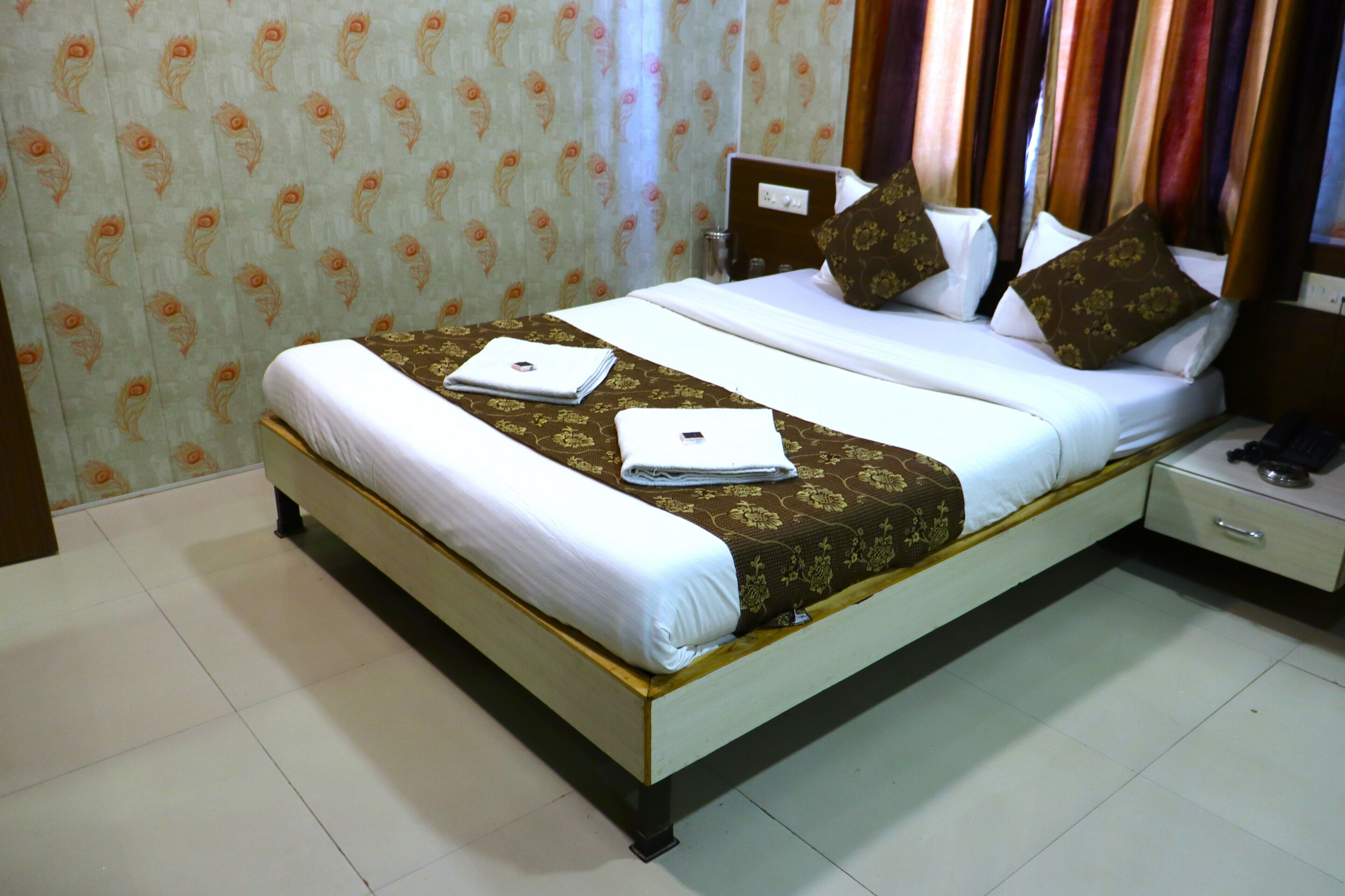 A hotel room with a bed, a nightstand, and a wall with patterned wallpaper.