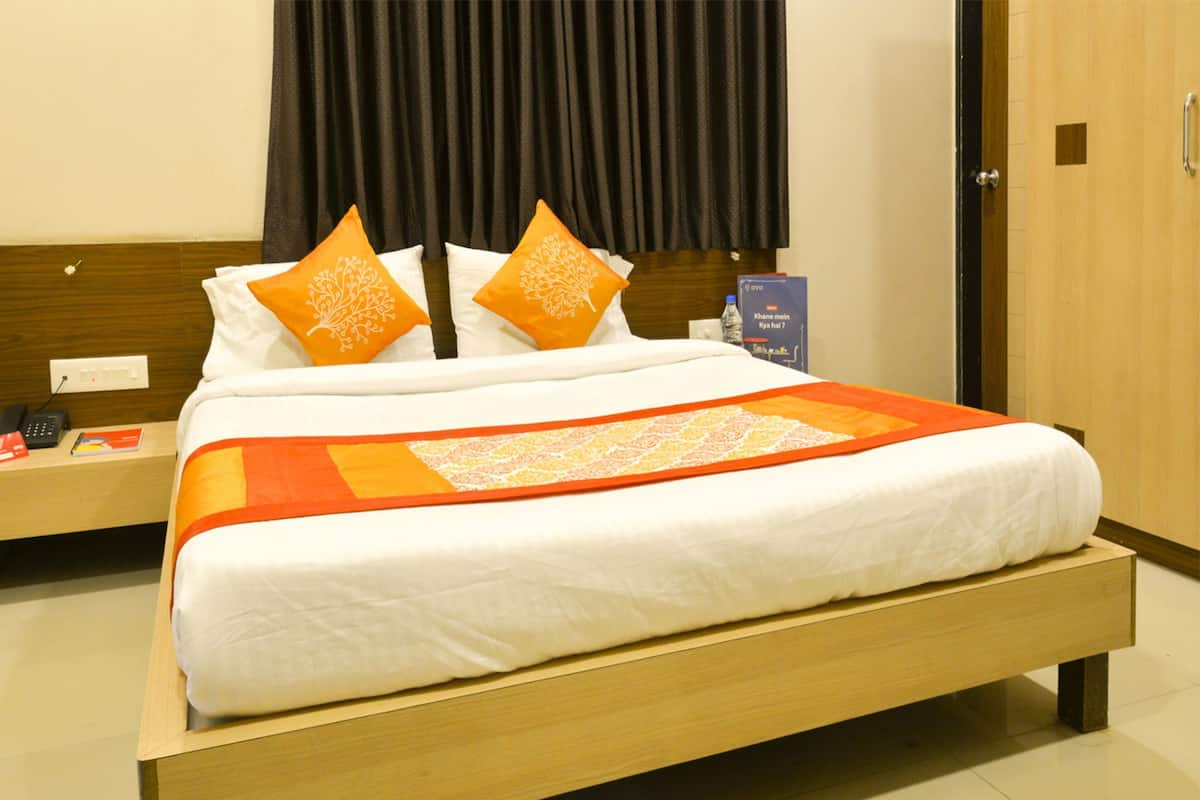 A hotel room with a wooden bed, white bedding, orange pillows, and a decorative orange and white blanket.