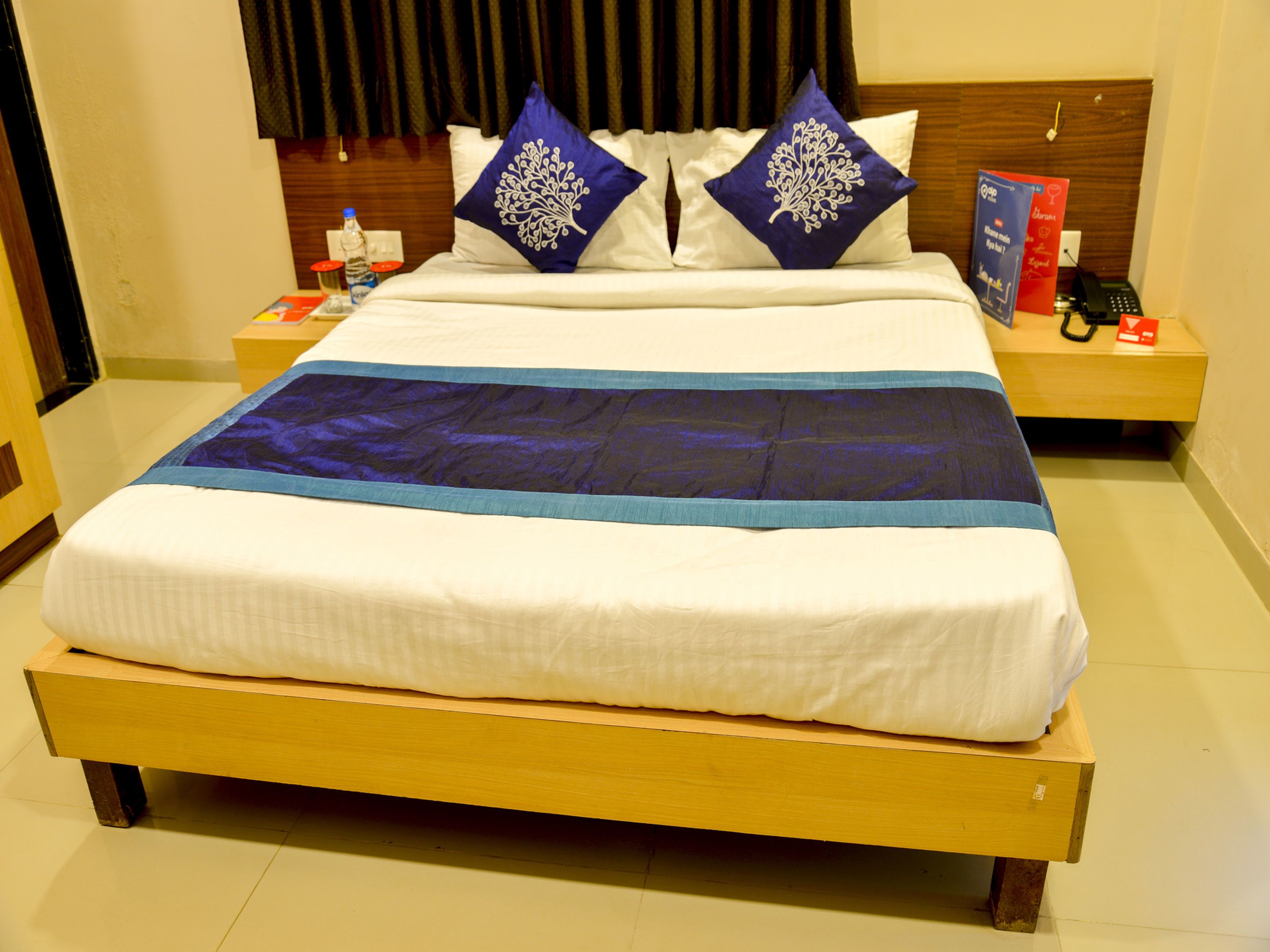 Ein ordentlich gemachtes Bett mit einer blau-weißen Tagesdecke, zwei Zierkissen und einem Holz-Kopfteil.