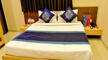 Ein ordentlich gemachtes Bett mit einer blau-weißen Tagesdecke, zwei Zierkissen und einem Holz-Kopfteil.