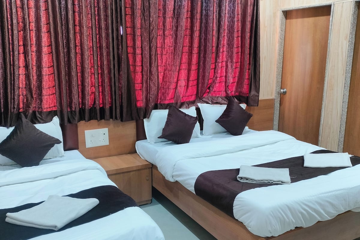 A hotel room with two beds, wooden headboards, and red curtains.