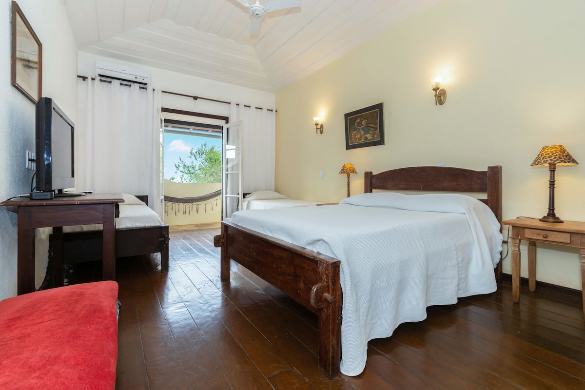 Une chambre d’hôtel avec un lit en bois, un bureau avec un ordinateur, une chaise rouge et une fenêtre avec des rideaux.