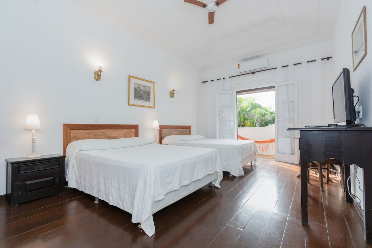 Une chambre d’hôtel avec deux lits, un bureau, une télévision et un balcon donnant sur un espace verdoyant.
