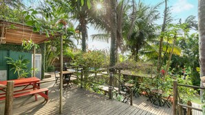 Eine Holzterrasse mit Picknicktischen und -stühlen, umgeben von üppigem Grün und Palmen.