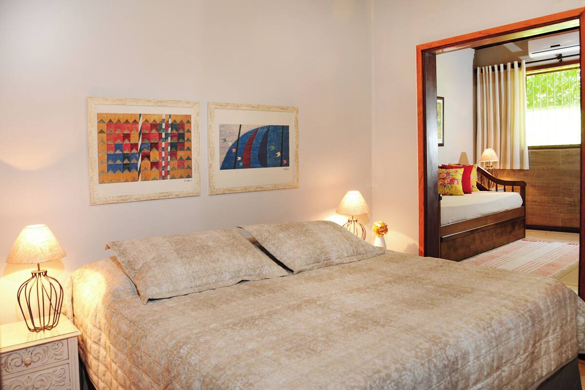 A bedroom with a bed, two bedside lamps, and two framed artworks on the wall.