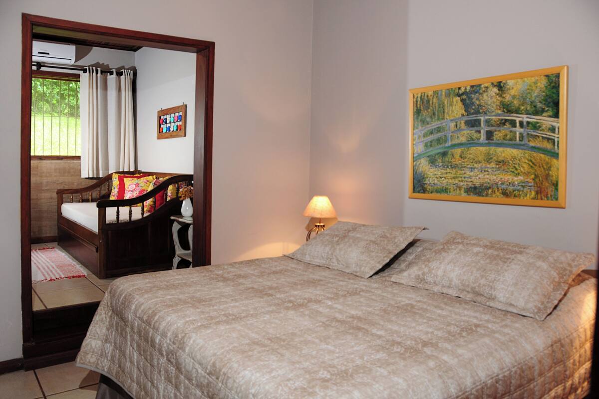 A bedroom with a bed, a nightstand, a lamp, a painting, and a window with curtains.