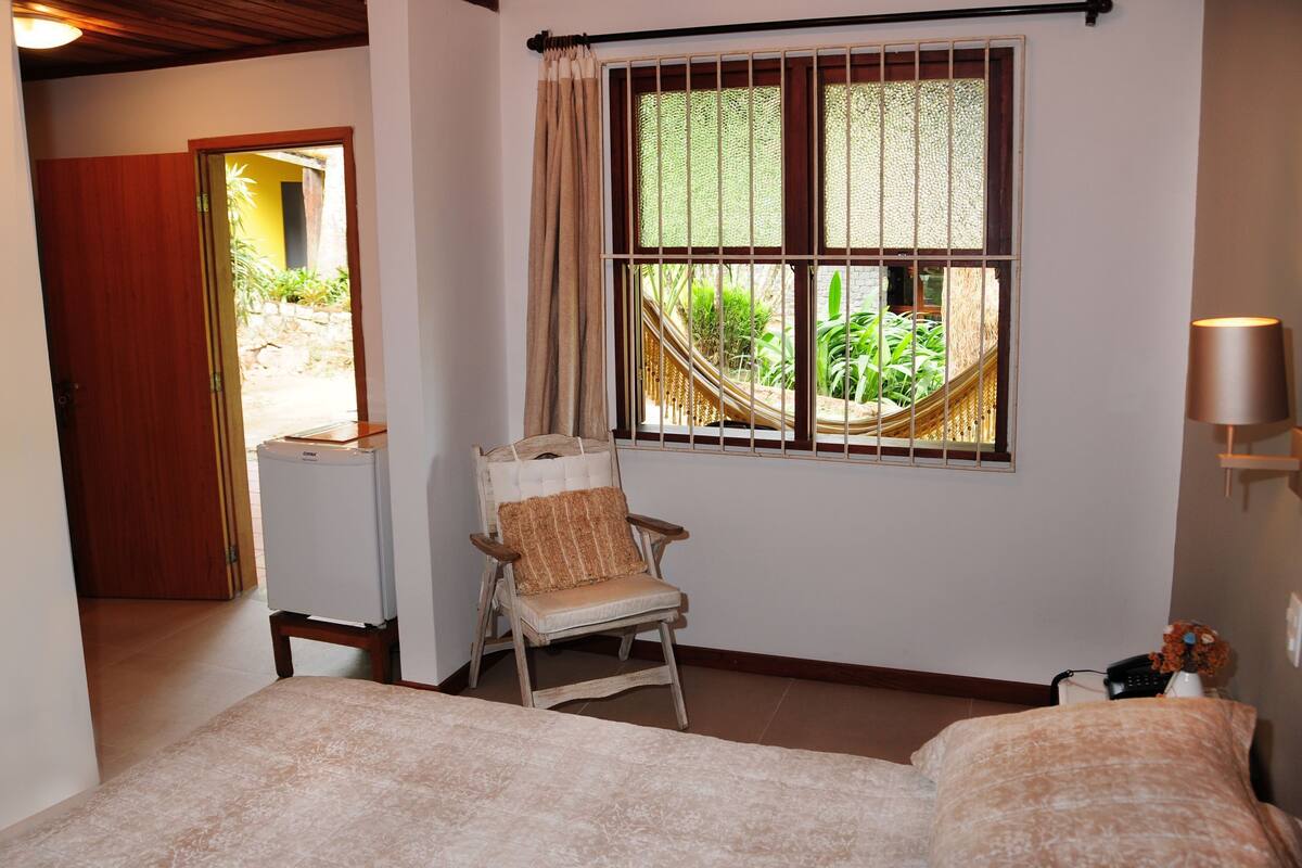 A bedroom with a bed, a chair, a TV, a window with a view, and a lamp.