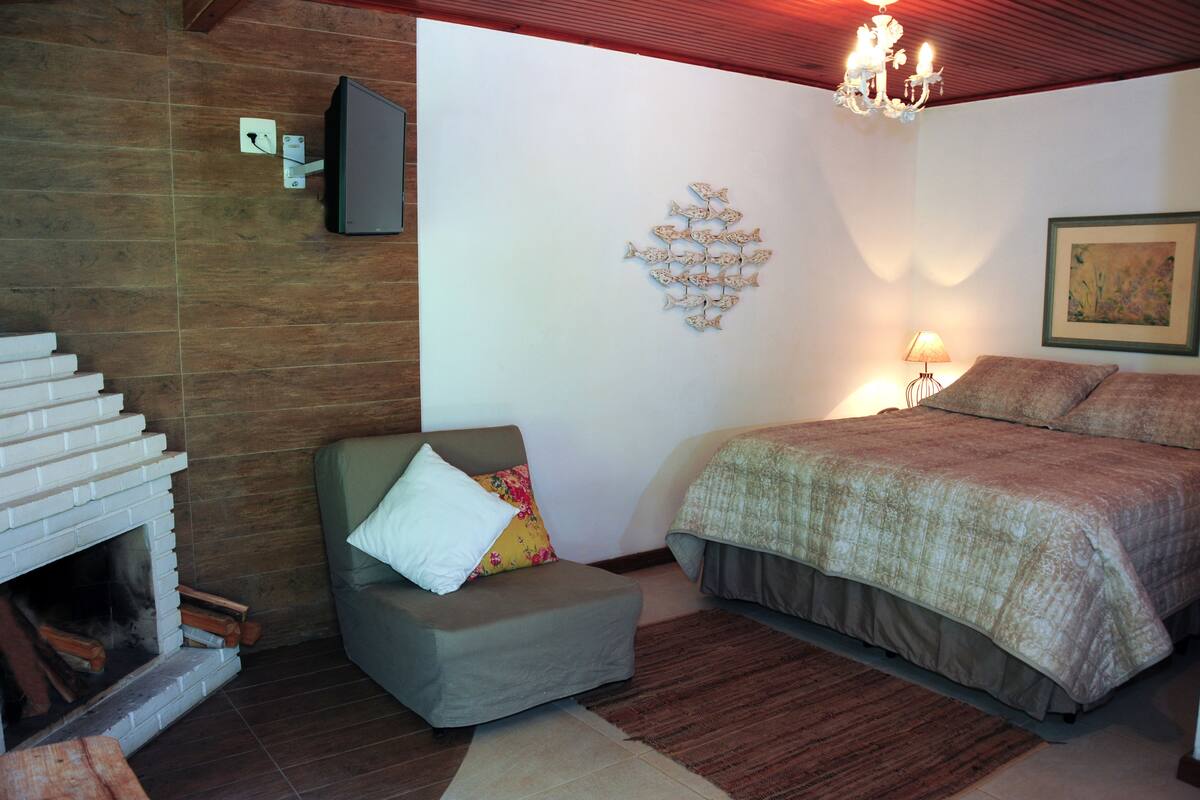A bedroom with a fireplace, a bed, a sofa, and a chandelier.
