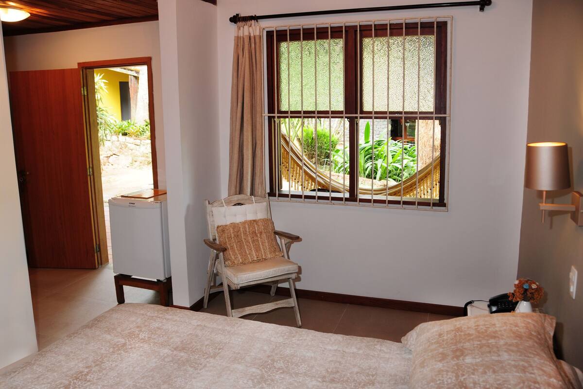 A bedroom with a bed, a chair, a television, and a window with a view of greenery.