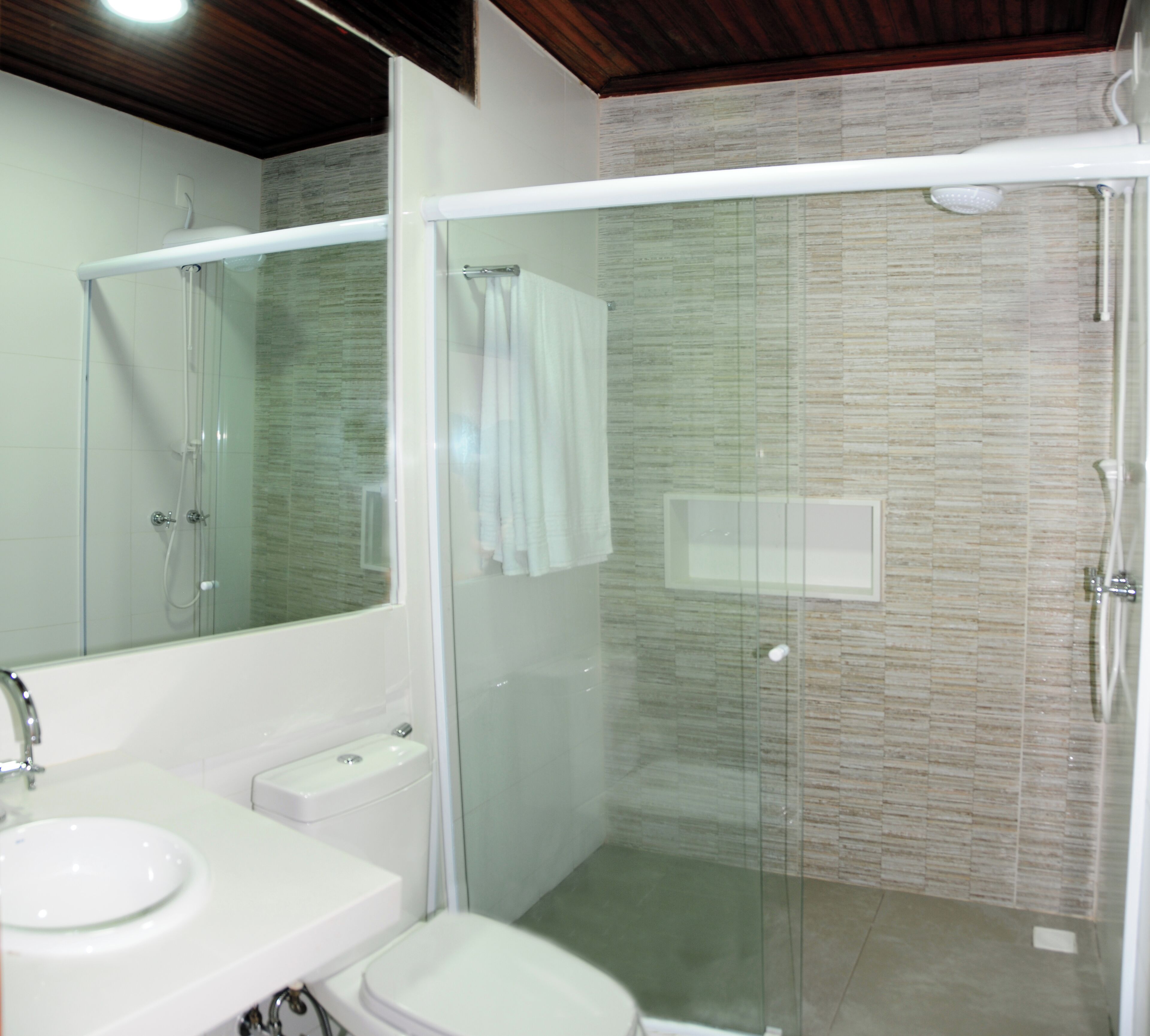Un baño moderno con ducha envuelta en vidrio, un lavamanos blanco y un inodoro.