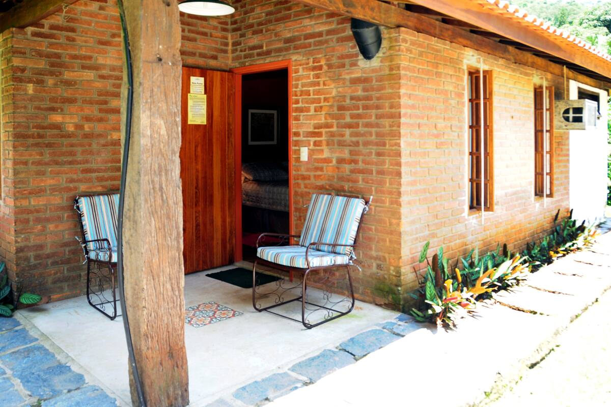 A brick building with a wooden door, two striped chairs outside, and a small garden area.