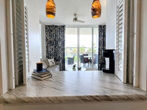 A spacious living area with a sofa, a coffee table, and a television. There are two pendant lights and a ceiling fan. The room has large windows with patterned curtains. - V310 Cozy Gulf View Villa w/Private Balcony Washer/Dryer & Free Beach Chairs (Fort Walton Beach)