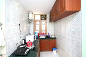 A small kitchen with a microwave, kettle, and various kitchen utensils. There are wooden cabinets and a tiled backsplash. - OYO 10409 Home Cozy 4BHK New Shimla (Shimla)