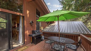 A wooden deck with a grill, outdoor table, chairs, and a green umbrella. - Vance by Hauserman Rentals (Tahoe City)