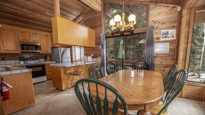 A wooden cabin with a kitchen featuring a stove, microwave, and refrigerator. There is a dining table with chairs and a chandelier. - Vance by Hauserman Rentals (Tahoe City)