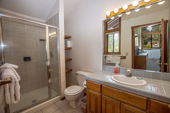 A bathroom with a glass shower enclosure, a toilet, a sink with a mirror above it, and wooden cabinets.