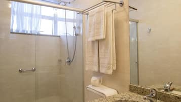 Un baño con ducha de vidrio, inodoro, lavamanos con encimera de granito y un espejo grande.