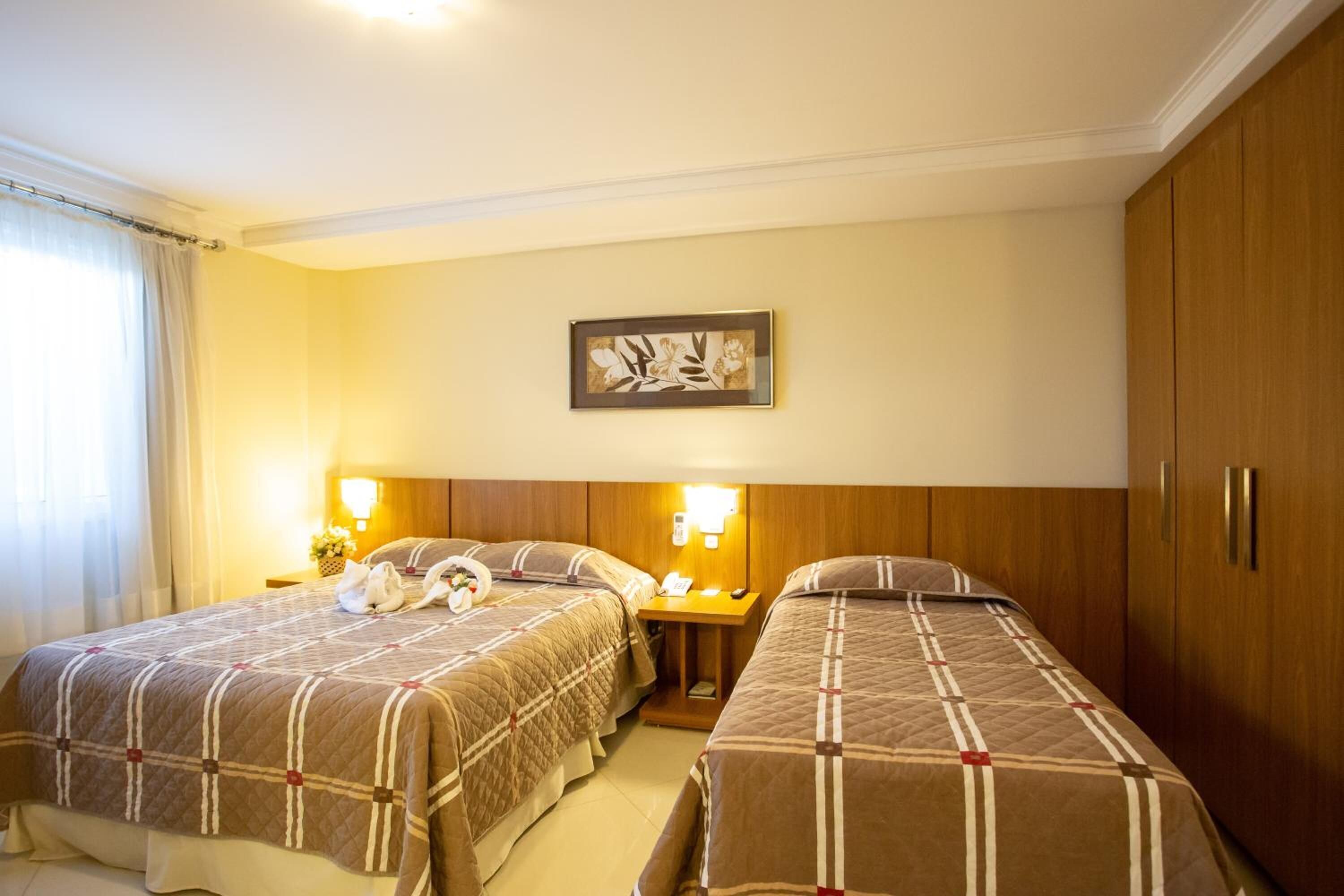 A hotel room with two beds, a wooden wardrobe, a framed artwork on the wall, and a nightstand with a lamp and a telephone.