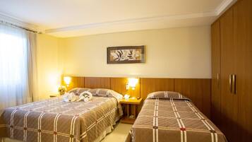 A hotel room with two beds, a wooden wardrobe, a framed artwork on the wall, and a nightstand with a lamp and a telephone.