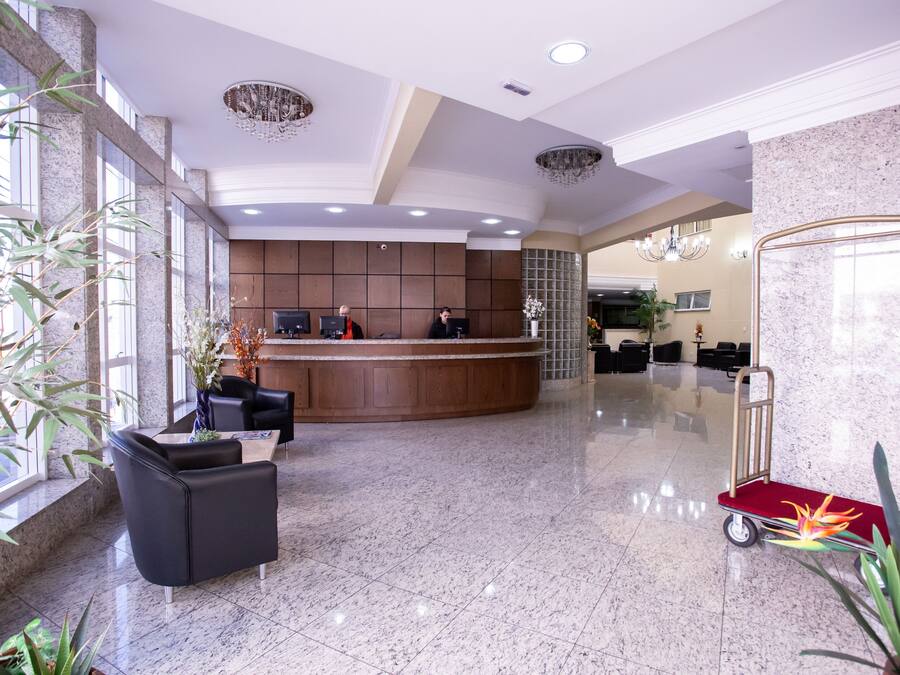 Un vestíbulo de hotel con mostrador de recepción, zona de estar y un carrito rojo.