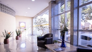 A lobby with a marble floor, a black leather chair, a reception desk, and potted plants. - Barbur Center Hotel (Ponta Grossa)